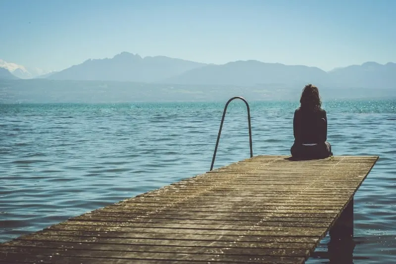 woman sitting on dock looking at lake