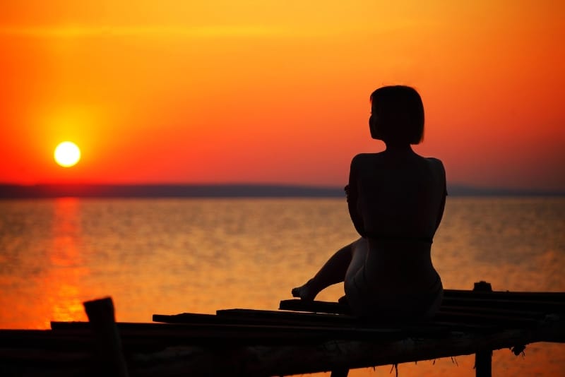 woman looking at sunset while sitting on dock