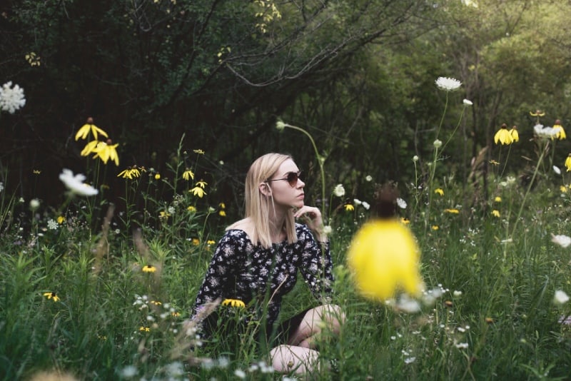 woman with sunglasses sitting on grass surrounded with flowers