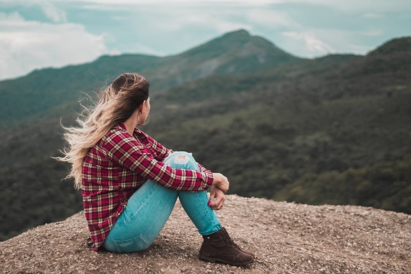 woman in checked shirt sitting on ground looking at mountain