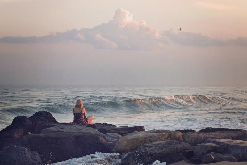 mujer sentada en una roca mirando al mar