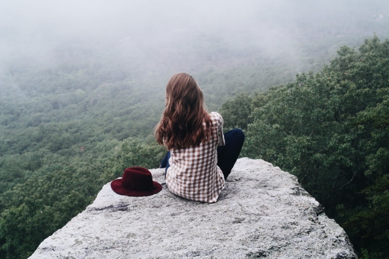 woman sitting on rock near red hat