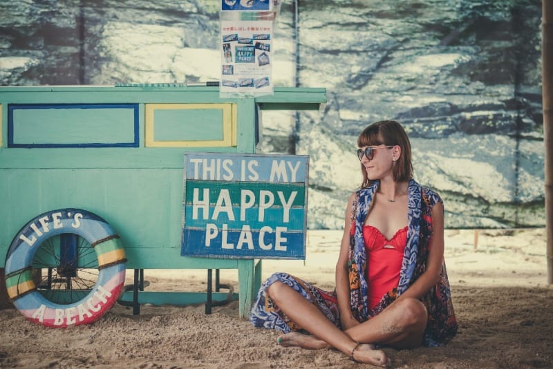 happy woman with eyeglasses sitting on sand