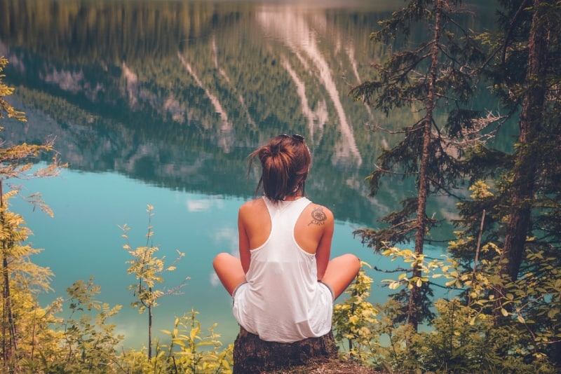 woman sitting on wood log looking at water