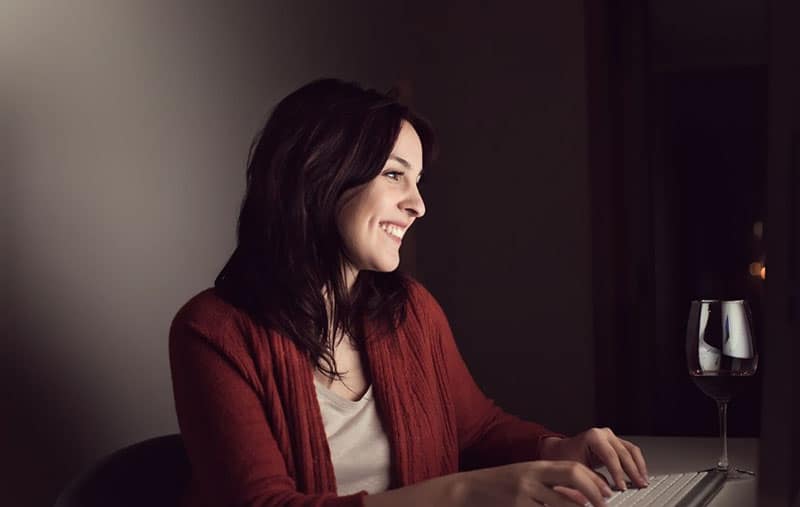 woman smiling while chatting online with a wine glass