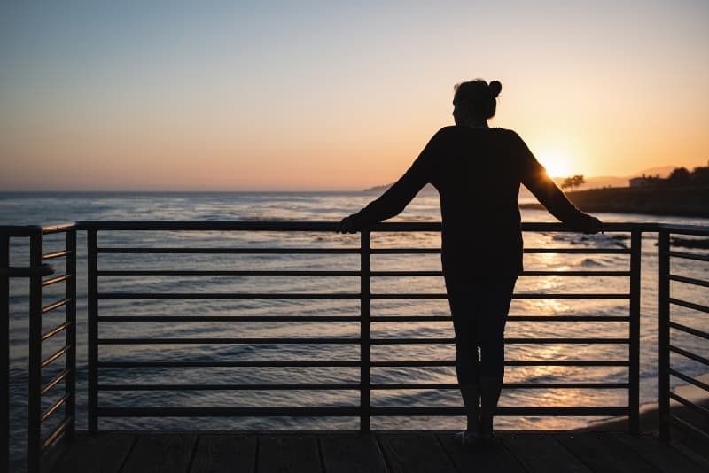 mulher de pé junto ao corrimão durante o pôr do sol