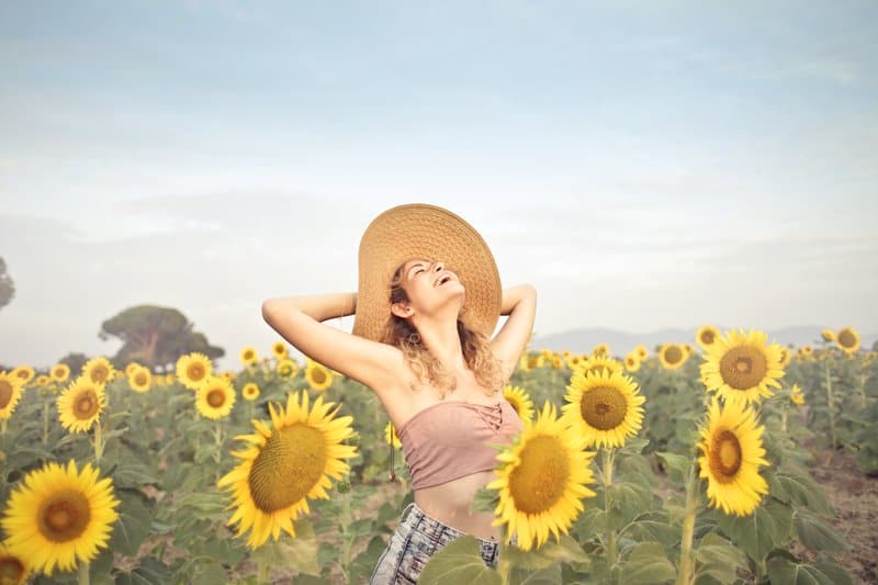 woman standing happily on the sunflower field wearing big hat and looking upwards