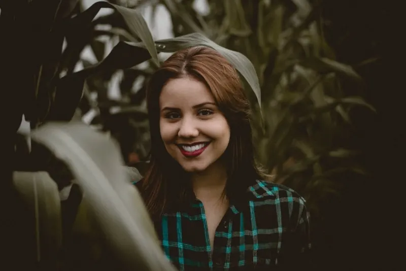 smiling woman in checked shirt standing in corn field