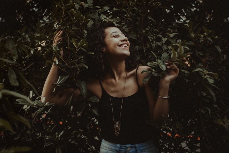 smiling woman in black top standing near bush