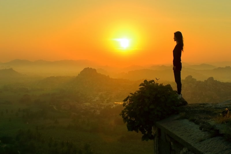 mulher de pé perto de um penhasco durante o pôr do sol