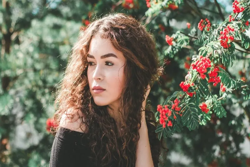 woman with curly hair standing near red flowers
