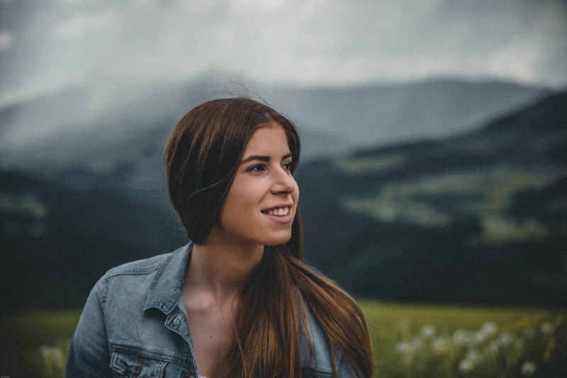 smiling woman in denim jacket standing near mountain