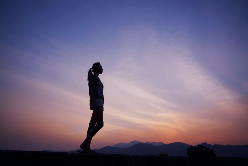 mulher de pé perto de montanhas durante o pôr do sol