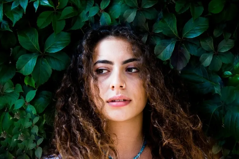 woman with curly hair standing near green plant