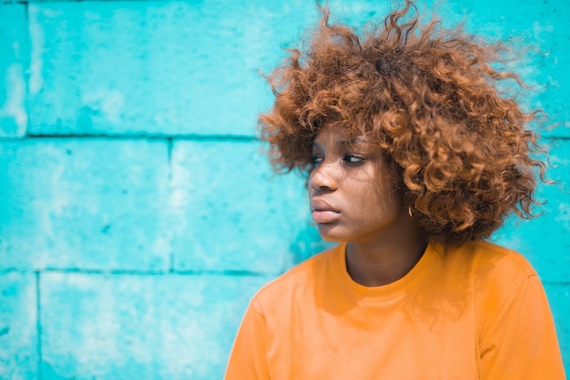 donna con capelli ricci in piedi vicino a un muro blu