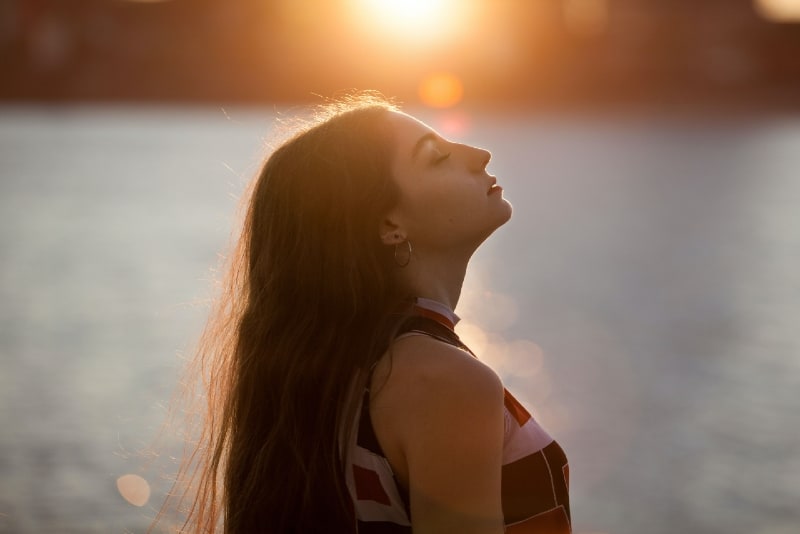 woman with eyes closed standing near water