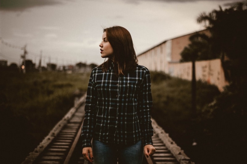 woman in checked shirt standing on train rail track