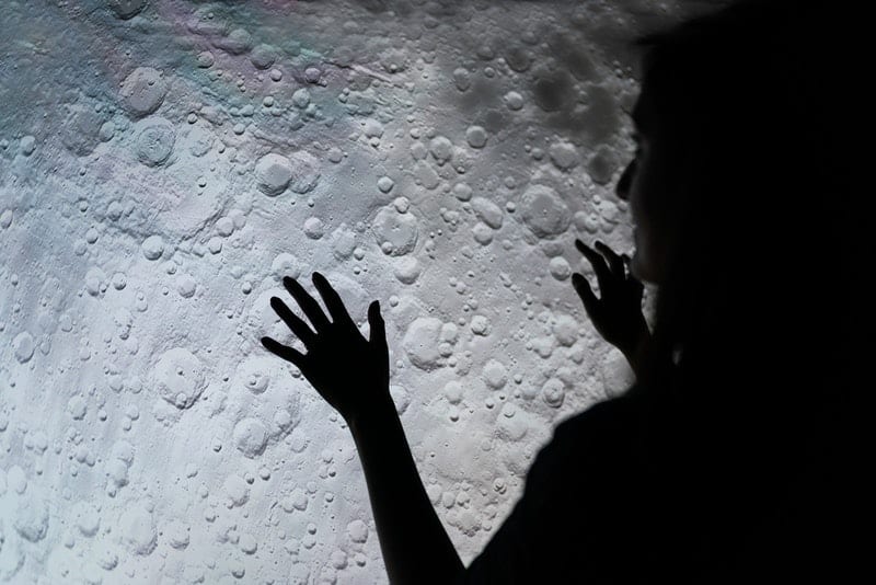 mujer estudiando y tocando la superficie de la luna en escala de grises