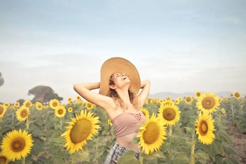 woman with hat standing surrounded by sunflowers