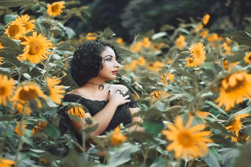 woman in black top standing surrounded with sunflowers