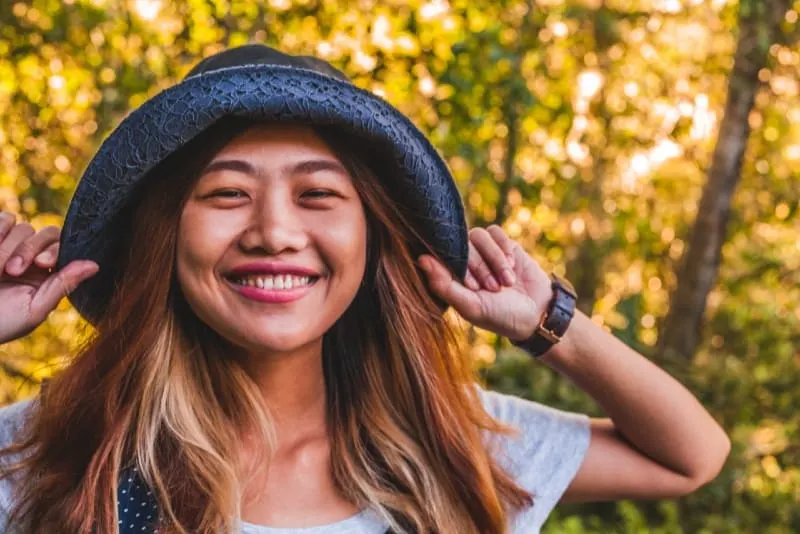 smiling woman touching her hat while standing outdoor