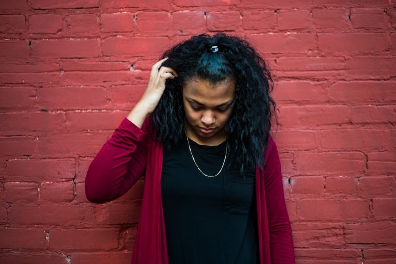 woman touching her hair while standing near red wall