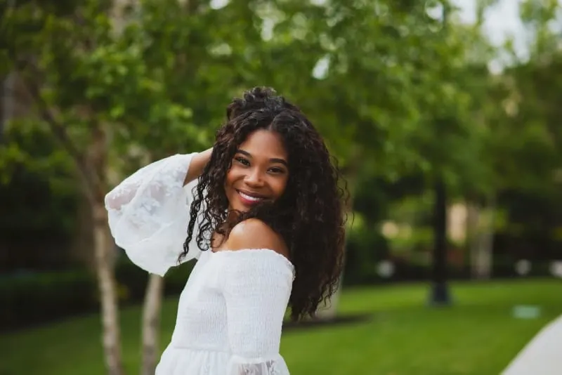 smiling woman in white dress touching her hair