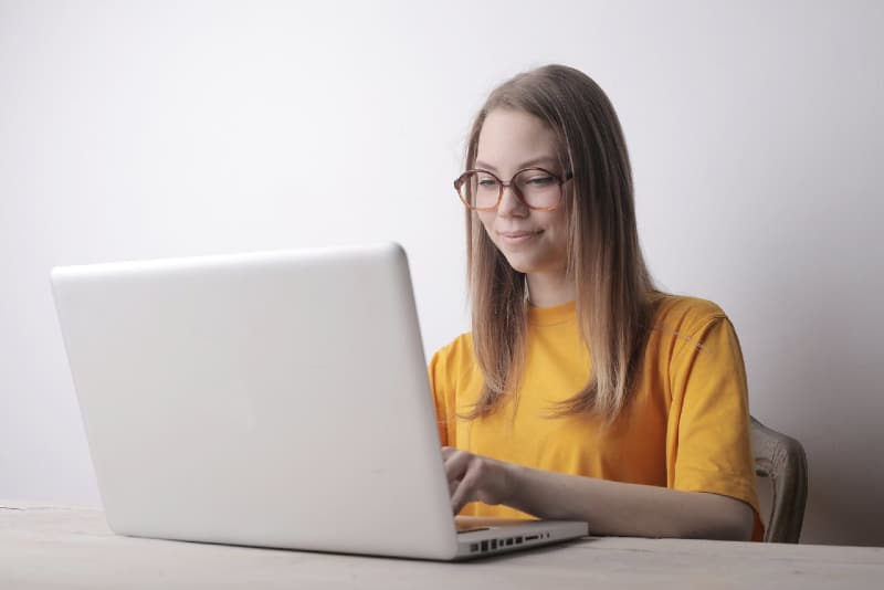 woman in yellow t-shirt using laptop while sitting at table