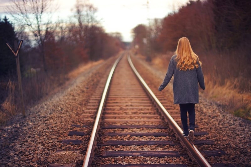 woman with gray coat walking on train track