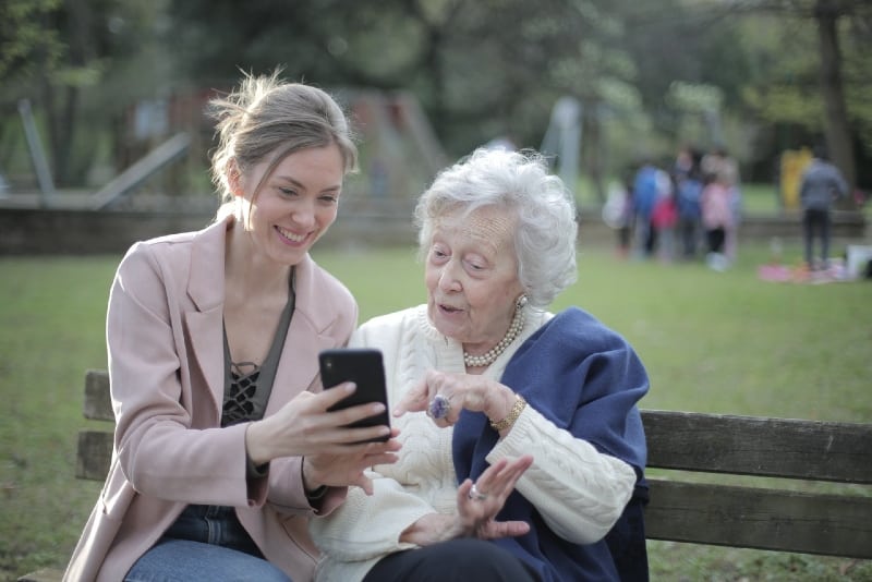 two women looking at phone while sitting on bench
