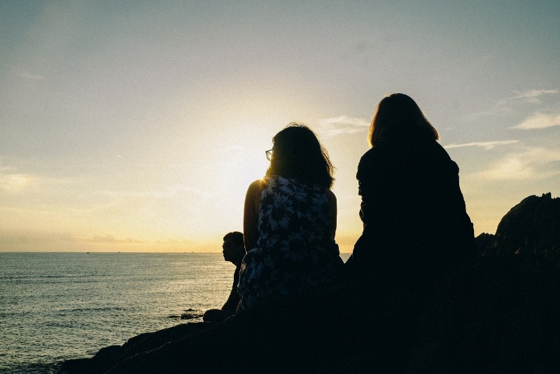 two women looking at sea during sunset