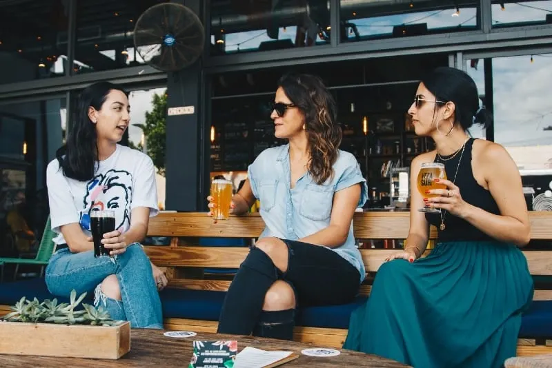 three women holding glasses of beer and talking