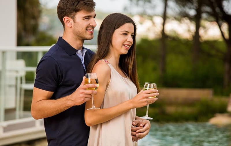 joven pareja cata de vinos de pie cerca de la piscina de un hotel