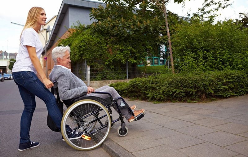 young woman helping an old person in the wheelchair to go over the streets ramp