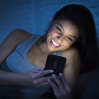 mujer sonriente usando el teléfono tumbada en la cama