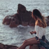 woman sitting on rock looking at ocean