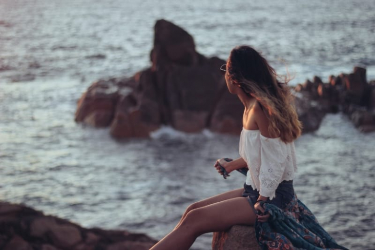 woman sitting on rock looking at ocean
