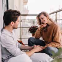 Ragazza caucasica che parla con il fidanzato che la tiene per mano mentre è seduta sul pavimento della terrazza