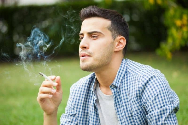 man smoking cigarette outdoors wearing blue checkered top