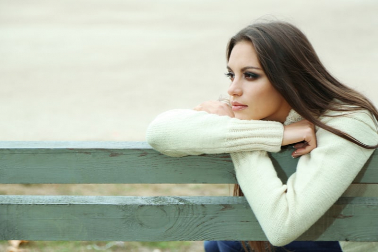 giovane donna sola su una panchina nel parco, seduta pensierosa