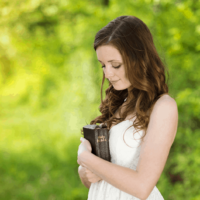 donna che porta una Bibbia vicino al cuore mentre si trova da qualche parte in un giardino verde