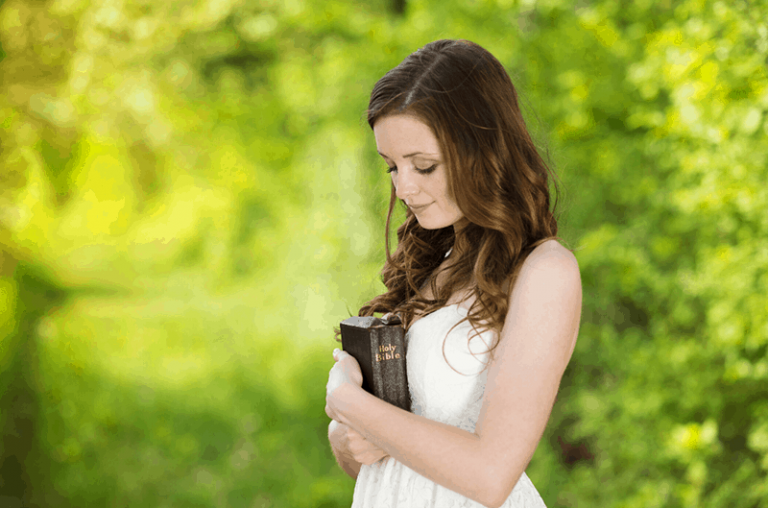 woman carrying a bible close to her heart while standing somewhere in a green garden