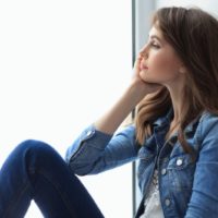 pensive woman wearing denim casual wear sitting by the big glass window