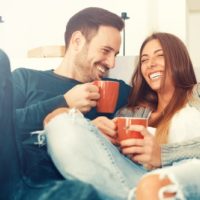 pareja feliz y alegre acurrucada en el sofá mientras toma café