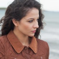 thoughful young curly black haired woman standing in the beach