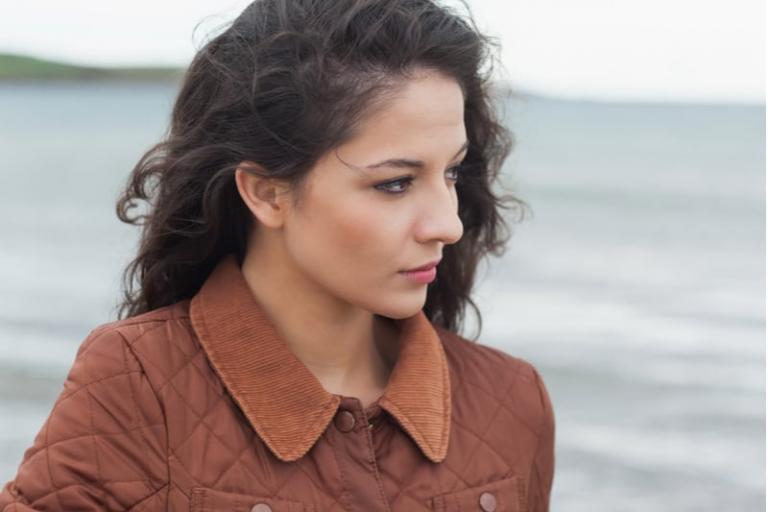 thoughful young curly black haired woman standing in the beach