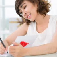 woman writing on white paper while sitting at table