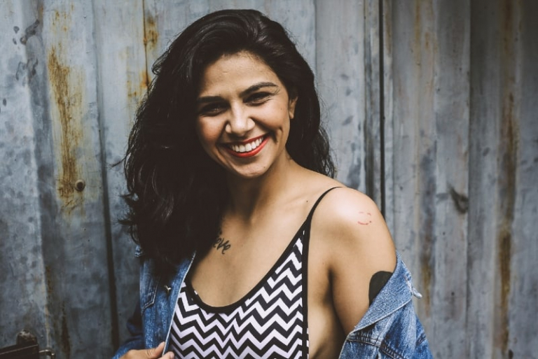 mulher sorridente, de top estampado, junto a uma parede