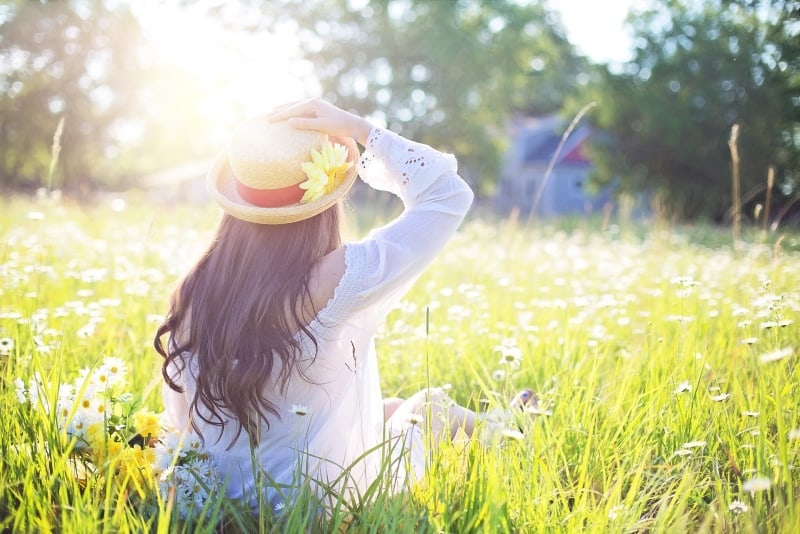 woman sitting on grass and touching her hat