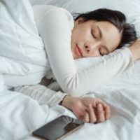 woman sleeping in bed near smartphone